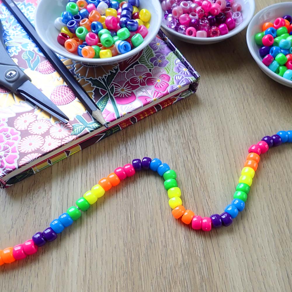 a strand of pony beads arranged on a craft table with bowls filled with pony beads