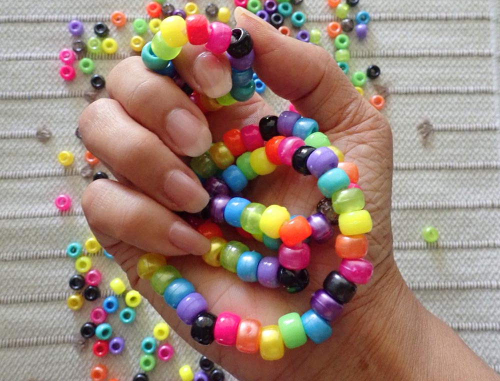 Hand holding bright pony bead strands with a textured surface background